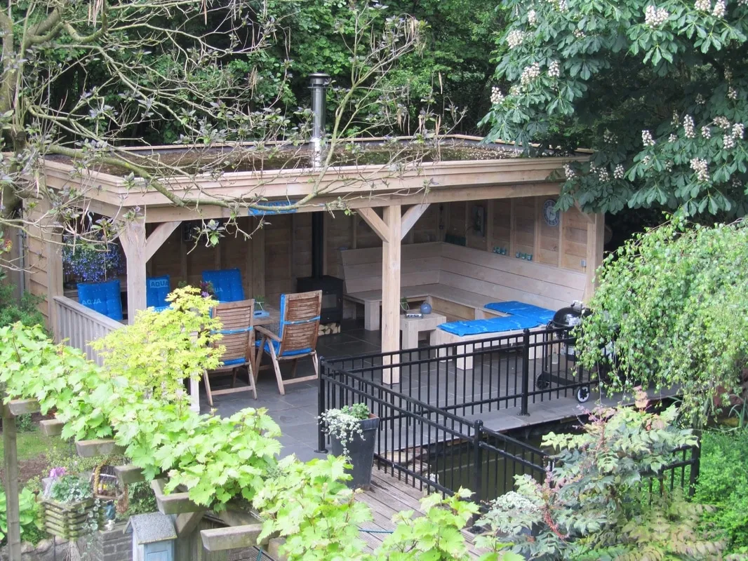 Overdekt buitenverblijf met zitplaatsen en kachel, omgeven door groen